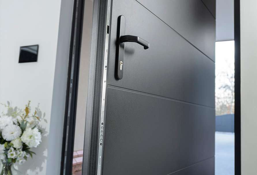 Anthracite aluminum entrance door ajar, showing the handle and multipoint lock strip
